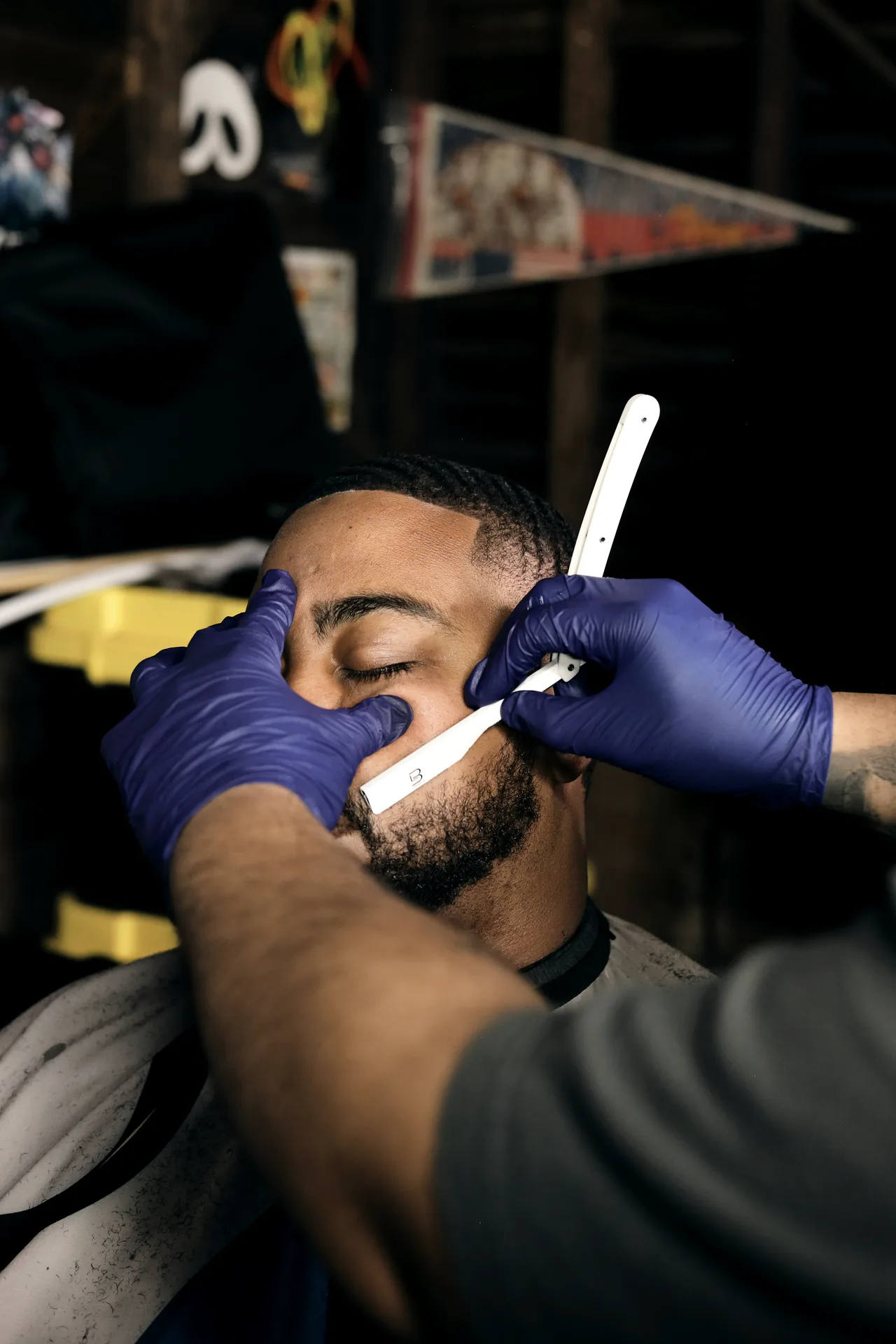 Barber in blue gloves lines up a client's beard with a straight razor