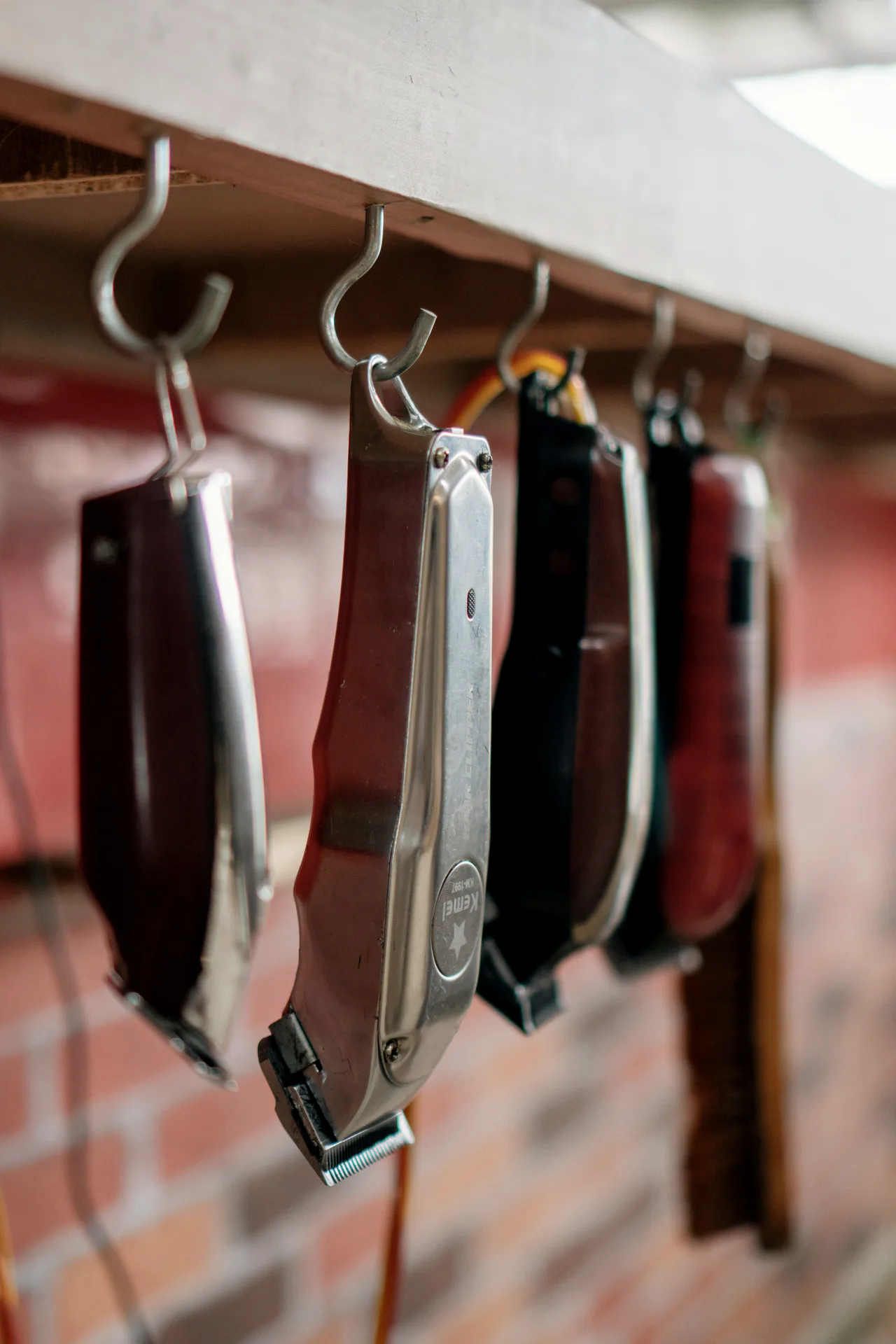 Row of clippers hanging from hooks against a red brick wall