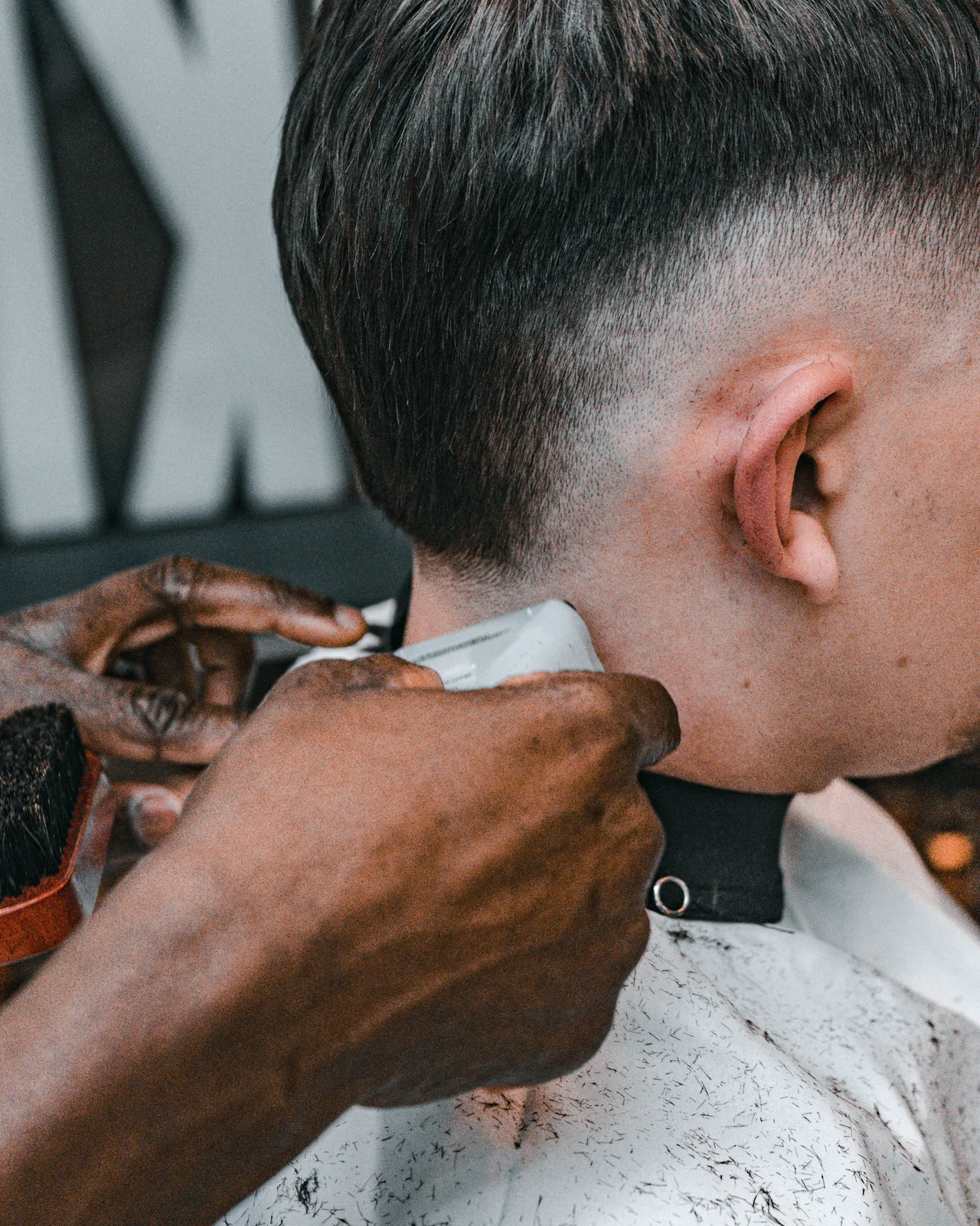 Barber's hands taper the neckline of a client's fade with clippers